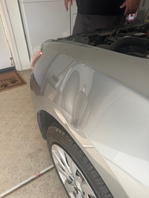 Silver car fender with dent before paintless dent repair