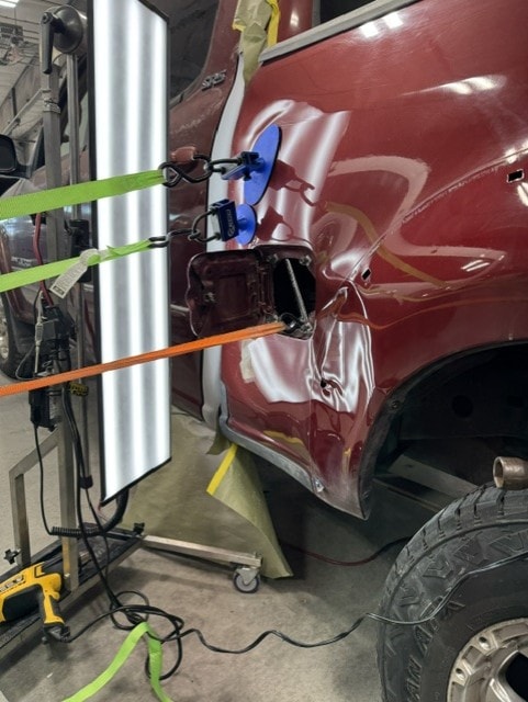 PDR technician working on a dark red truck fender with repair tools